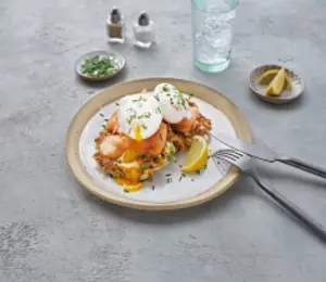 Potato and cheese fritters with salmon and poached eggs served on a round white plate